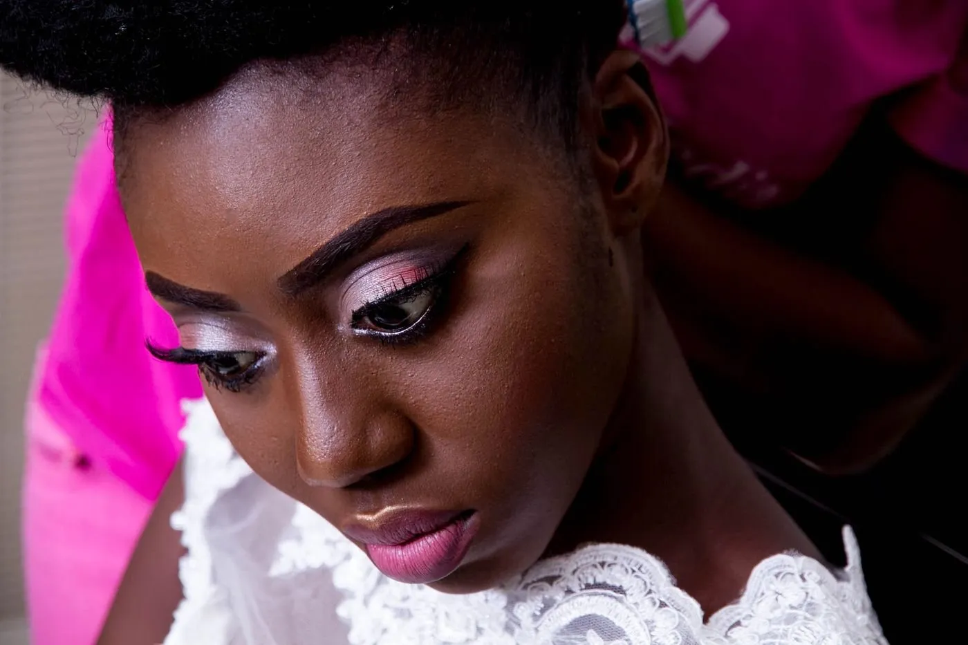 Bride with soft pink eye makeup and a lace gown, looking down